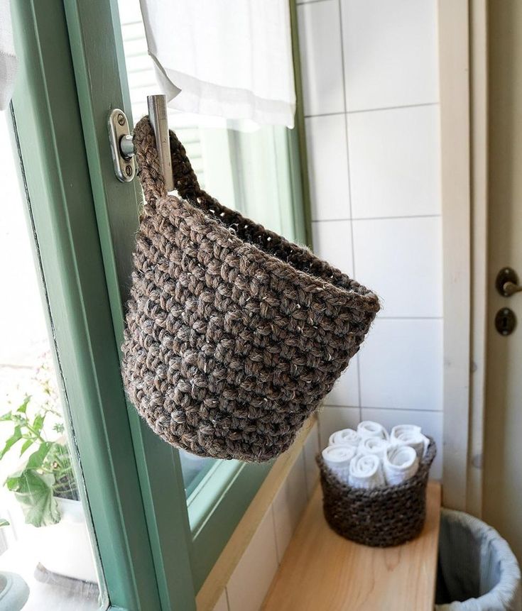 a basket hanging from the side of a door in front of a bathroom mirror with two rolls of toilet paper next to it