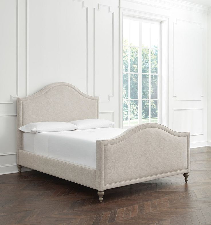 a white bed sitting on top of a hard wood floor next to a large window