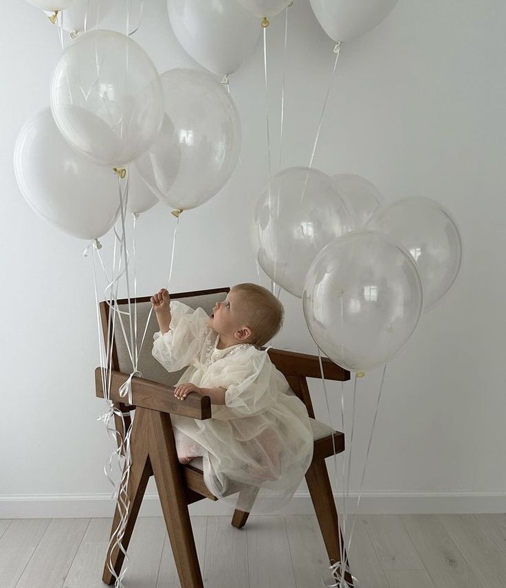 a baby sitting in a chair with white balloons