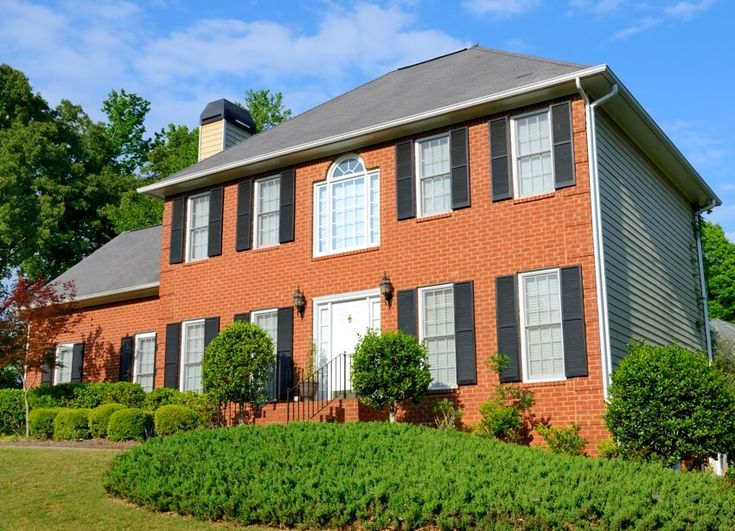 a red brick house with black shutters on the front and side windows is shown