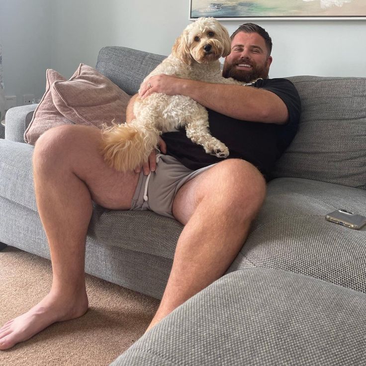 a man sitting on a couch with his dog in his lap and looking at the camera