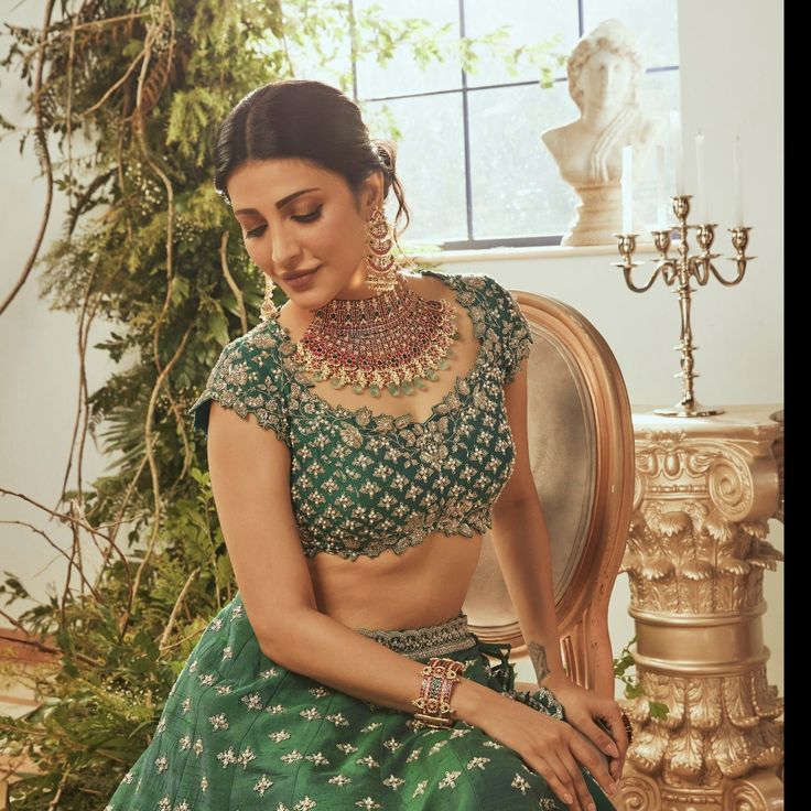 a woman sitting in a chair wearing a green lehenga and matching necklaces