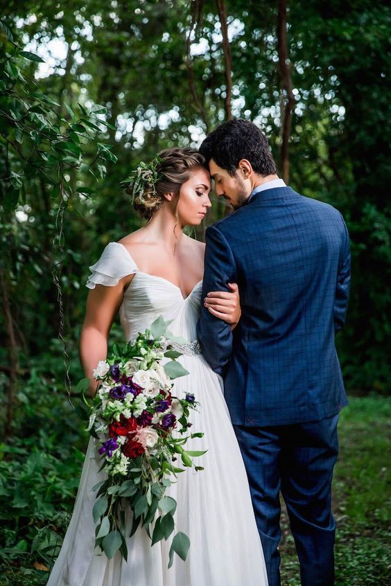 a man and woman standing next to each other in front of some trees with flowers