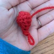 a small red crocheted heart in someone's hand