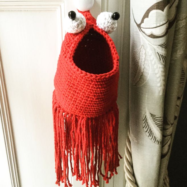 a crocheted red bag hanging from a door handle with eyes and nose on it