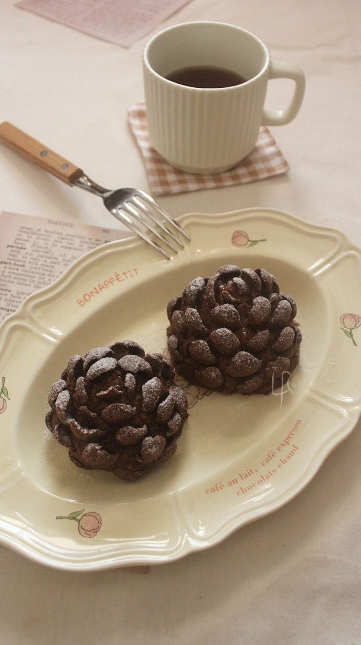 two chocolate cookies on a plate with a fork and cup of coffee in the background