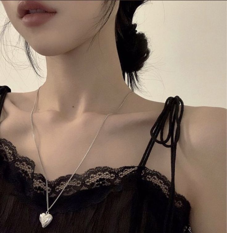 a woman wearing a black top with a heart pendant on her neck and an earring