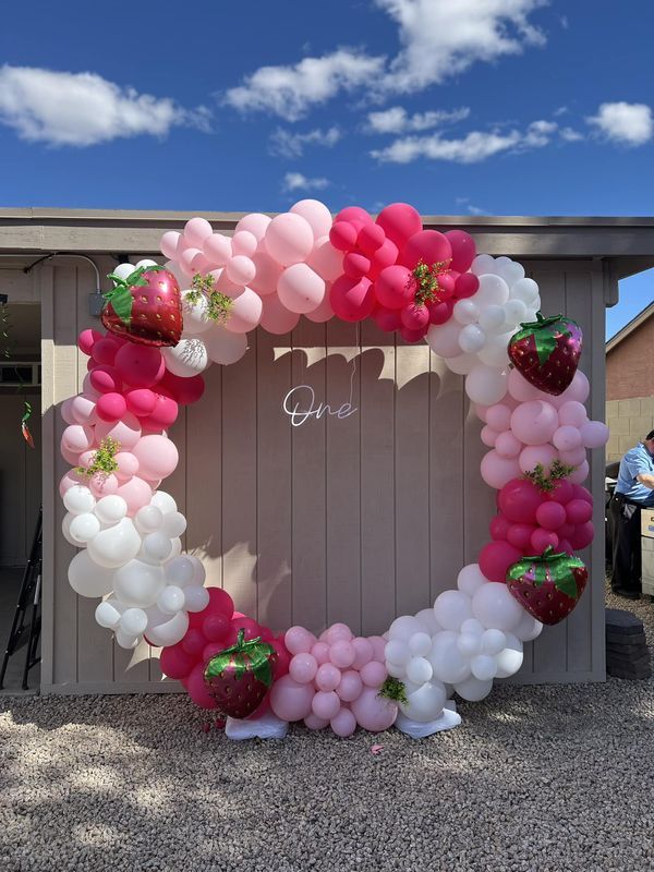 a heart shaped balloon wreath with strawberries and balloons attached to the front of a building