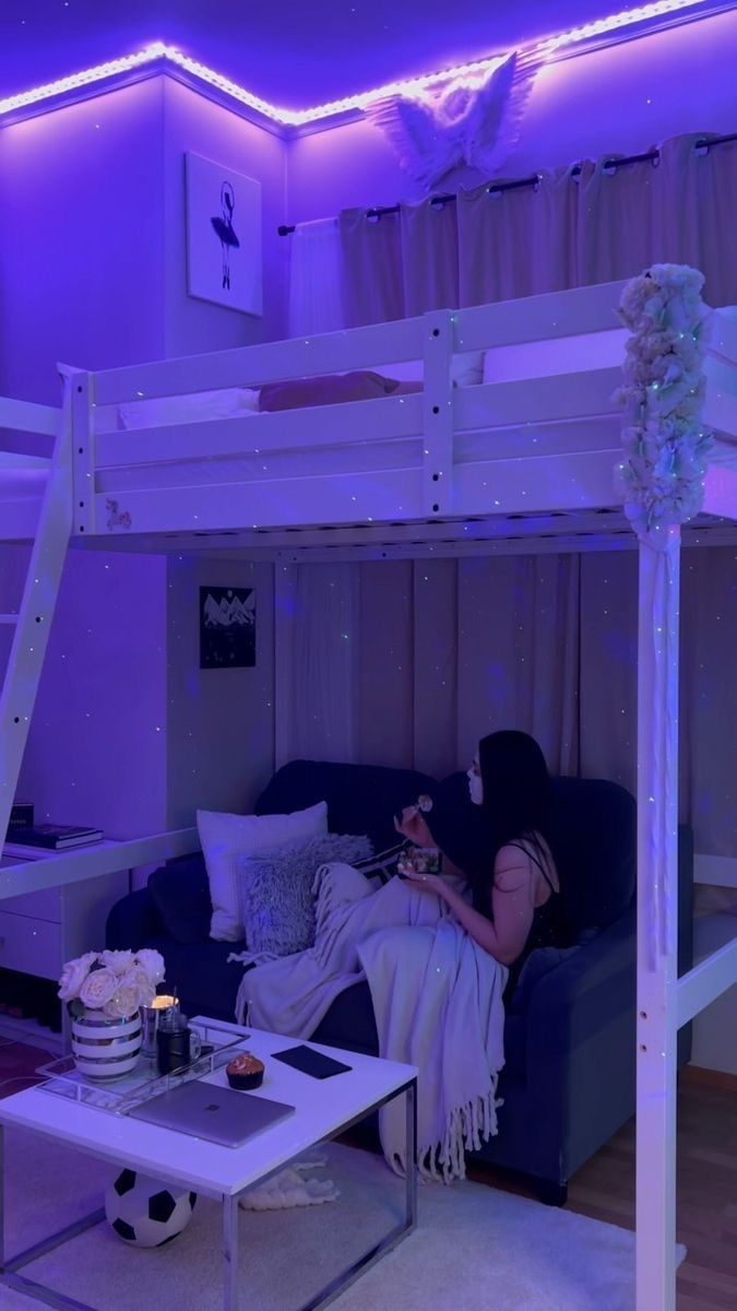 a woman sitting on top of a couch under a loft bed next to a table