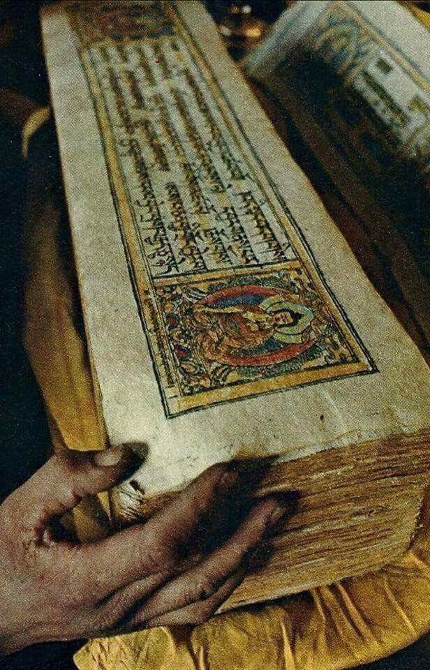 an old book being held by two hands over a table with other books on it