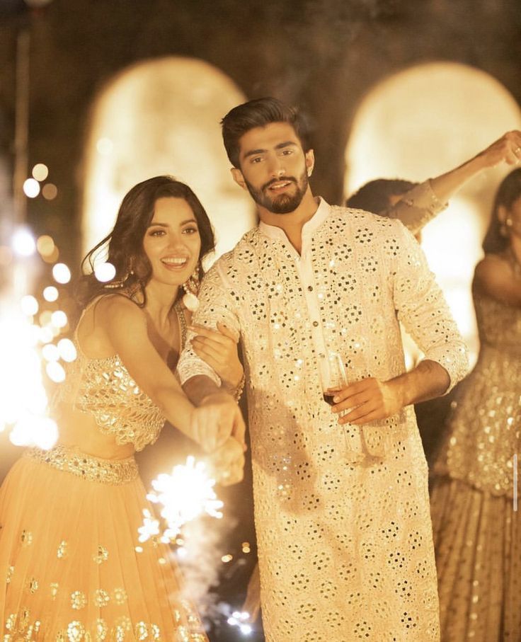 a man and woman standing next to each other with sparklers in the air behind them