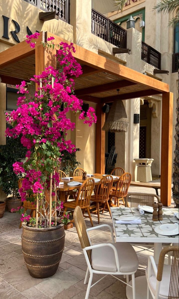 an outdoor dining area with tables, chairs and potted flowers on the table outside