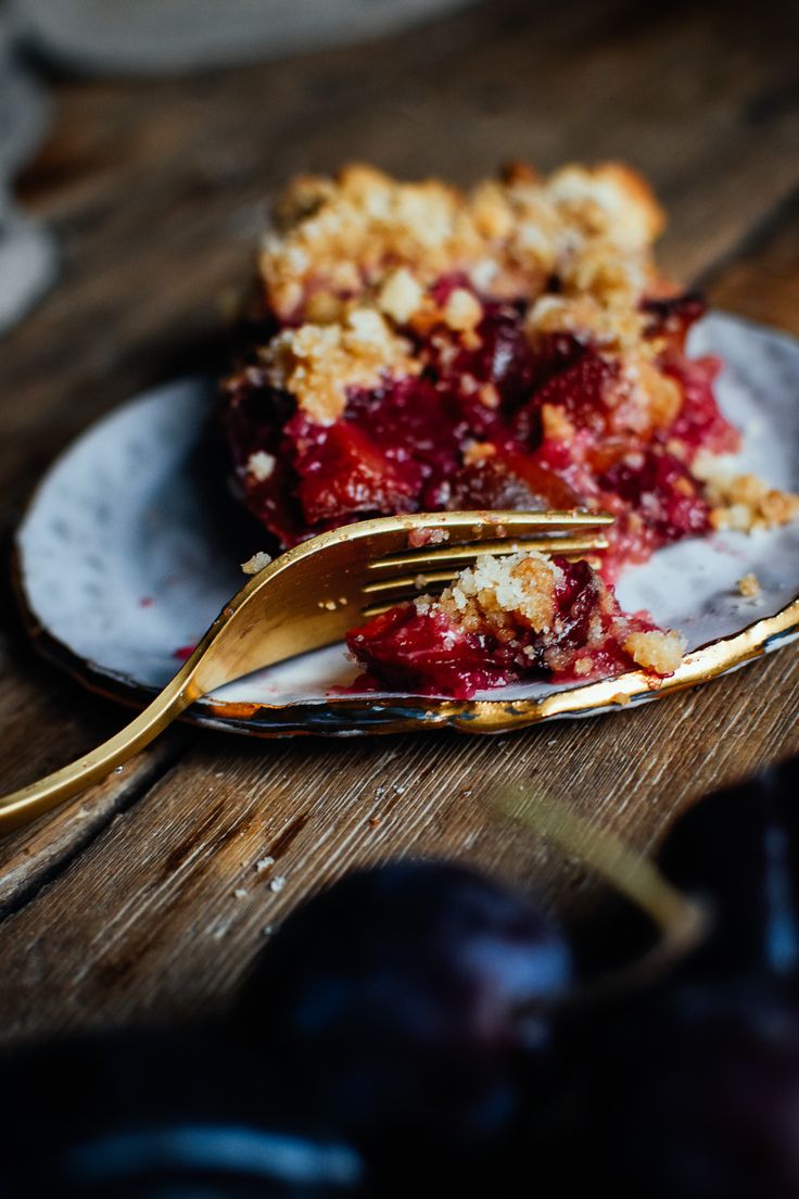 a piece of pie on a plate with a fork and some plums next to it