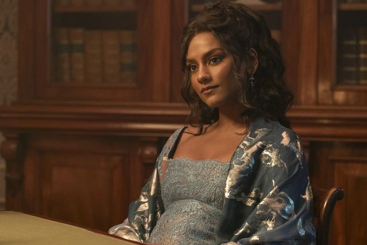 a woman sitting at a table in front of a bookcase wearing a blue dress