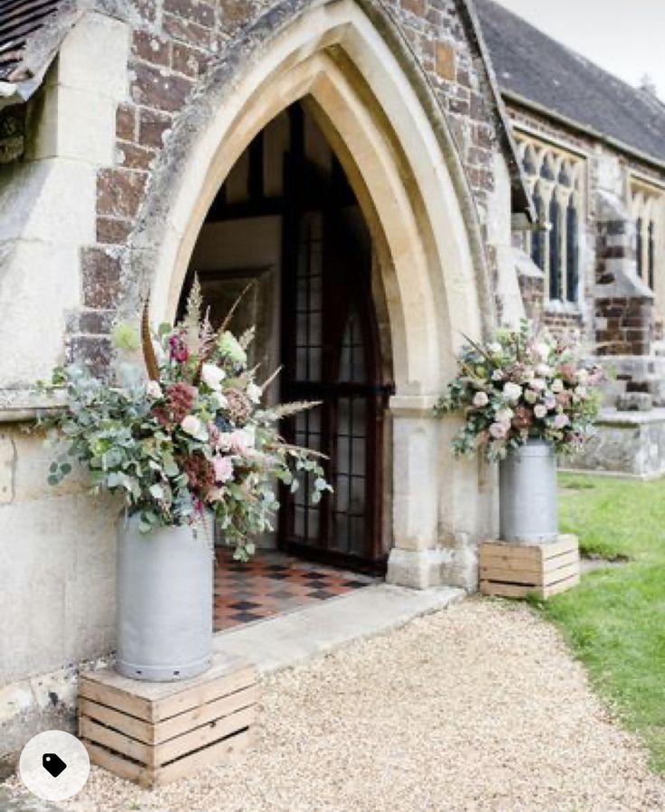 two tall vases with flowers are on the side of a church door, in front of an entrance