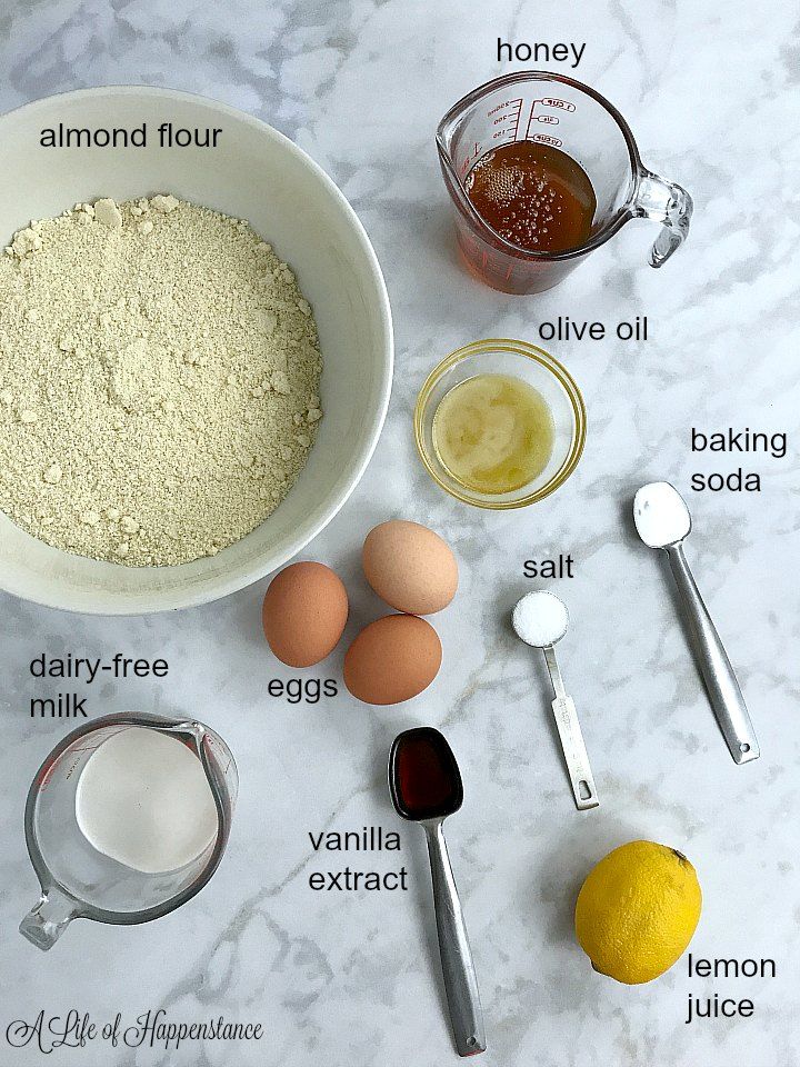 ingredients to make lemon muffins laid out on a marble counter top, including flour, eggs, butter, sugar and honey