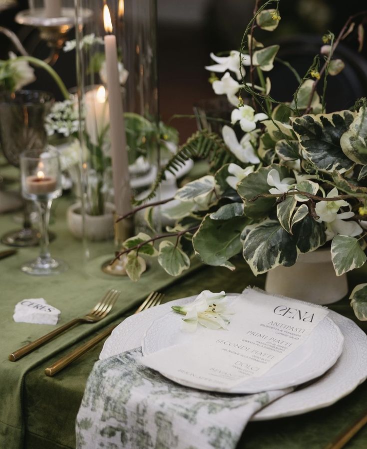 the table is set with plates, silverware and greenery for an elegant dinner