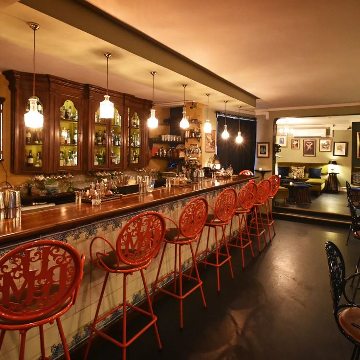 an empty bar with red chairs and wooden counter tops in a dimly lit restaurant area