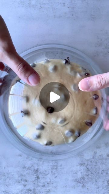 two hands reaching for an object in a bowl with chocolate chip cookies on the bottom