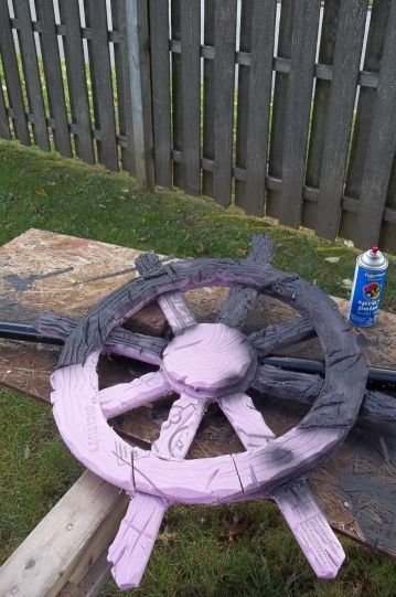 a purple painted wheel on the ground next to some wood planks and a can of paint