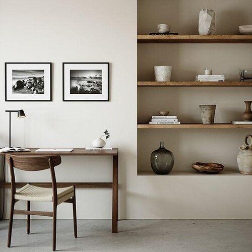 a desk and chair in a room with shelves on the wall above it, along with two vases