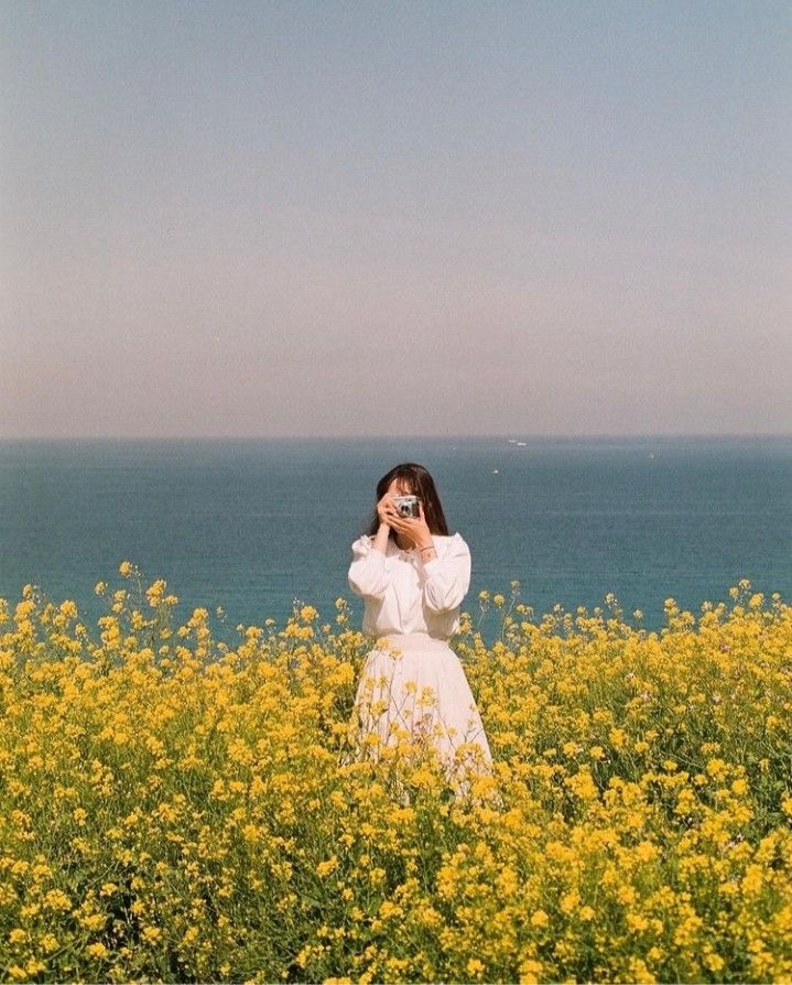 a woman in a white dress is standing in a field with yellow flowers and looking into the distance