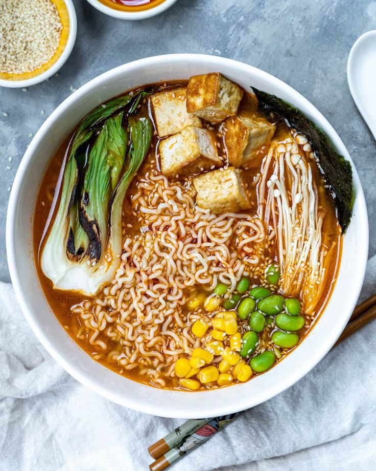 an overhead view of a bowl of ramen soup with vegetables and tofu on the side