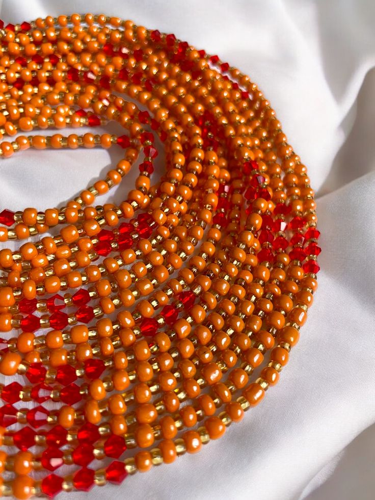 "Oupoyo" – a Single Strand Waist Bead that brings together the rich warmth of orange crystal glass seed beads and the subtle opulence of gold glass seed bead accents. ✨ Vibrant Orange Radiance: Oupoyo exudes a radiant glow with its vibrant orange crystal glass seed beads, reflecting the energy of the sun and infusing your ensemble with a lively and spirited charm. 🌟 Gold Opulence: Interspersed among the beads are golden accents, evoking a sense of opulence and sophistication. The gold glass see Strong Hand, Orange Crystals, Waist Beads, Glass Seed Beads, Gold Glass, Vibrant Orange, Green Crystals, Deep Green, How To Make Beads