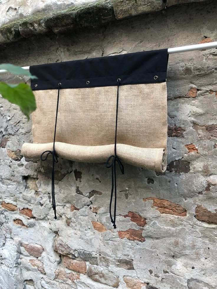 a bag hanging on a clothes line next to a stone wall with a plant growing out of it