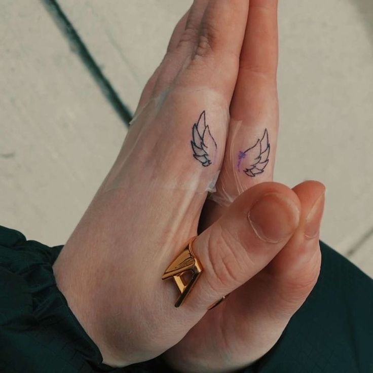 two fingers with small tattoos on them, one is holding the other's hand