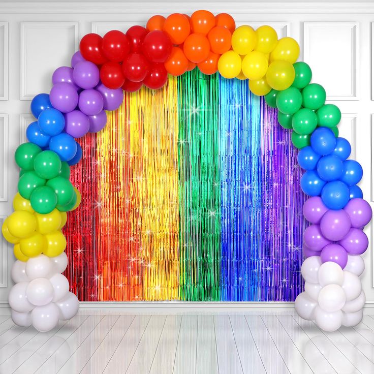 a rainbow arch with balloons and streamers on the floor in front of a white wall