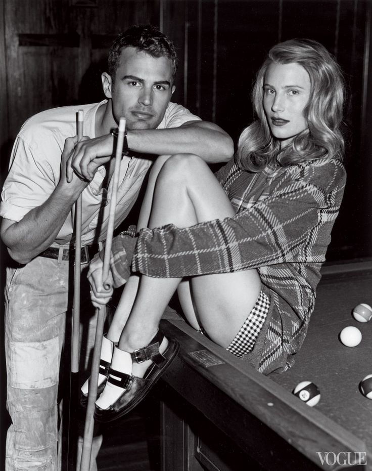 black and white photograph of man and woman with pool cues sitting on the table