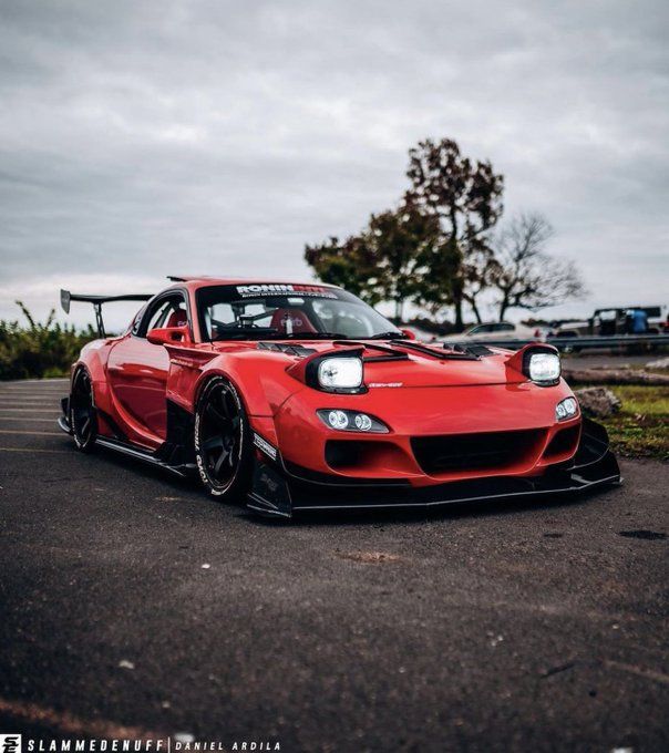 a red sports car parked in a parking lot next to a tree and cloudy sky