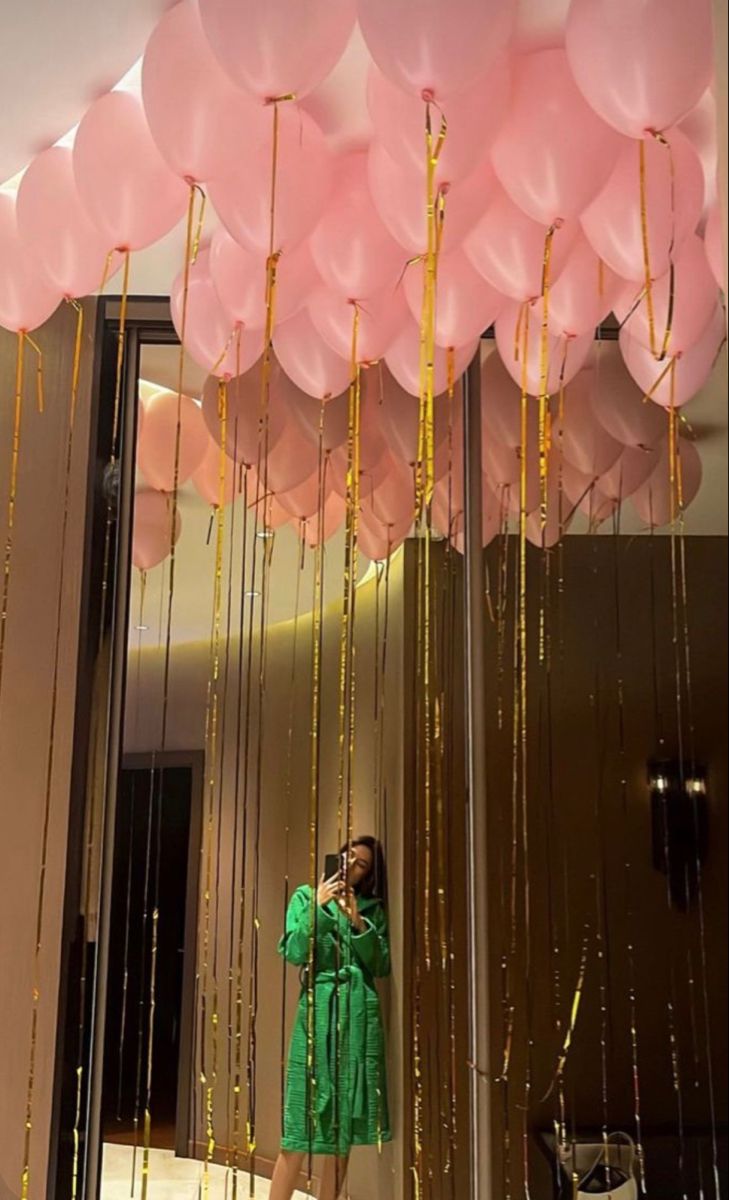 a woman in a green dress taking a photo with her cell phone and balloons hanging from the ceiling