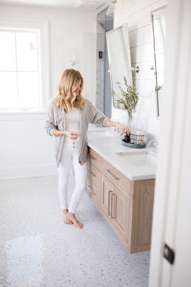 a woman standing in front of a bathroom sink holding a cup and looking at the mirror