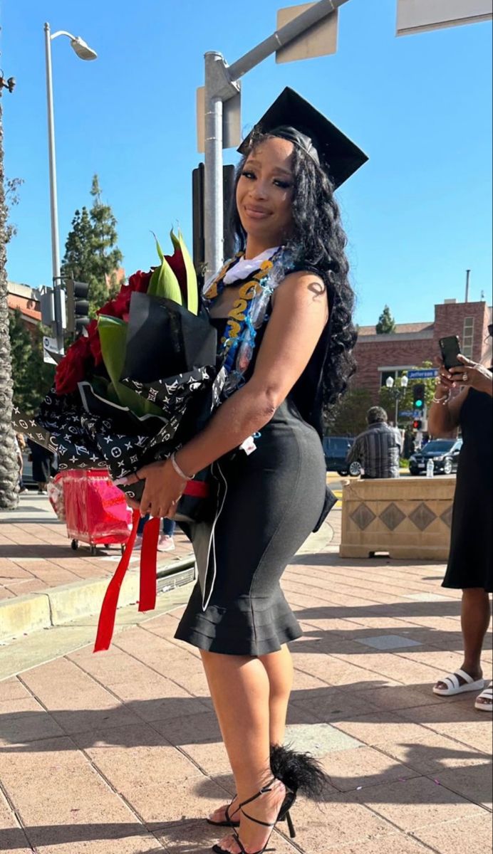 a woman is holding flowers and wearing a graduation cap