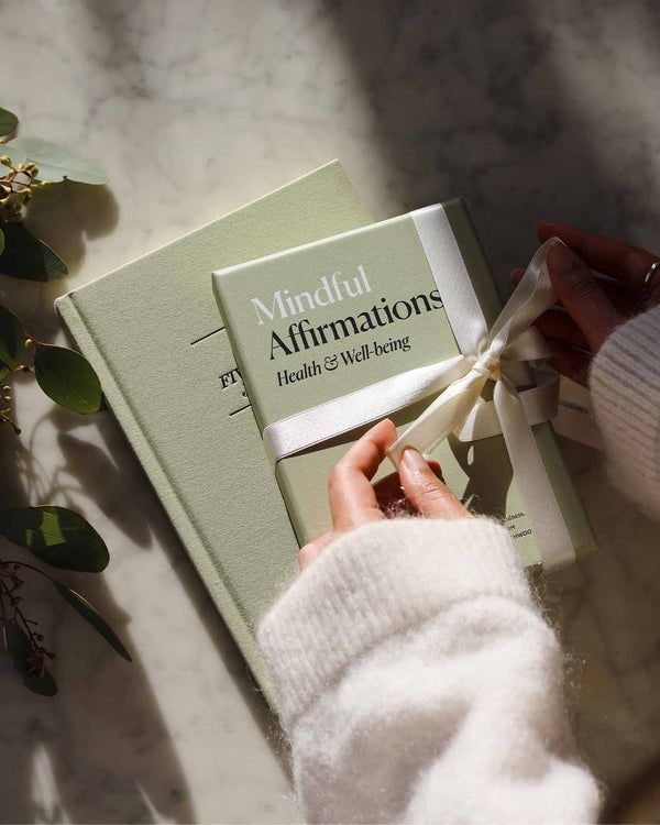 a person is holding onto a book on the table next to some plants and flowers