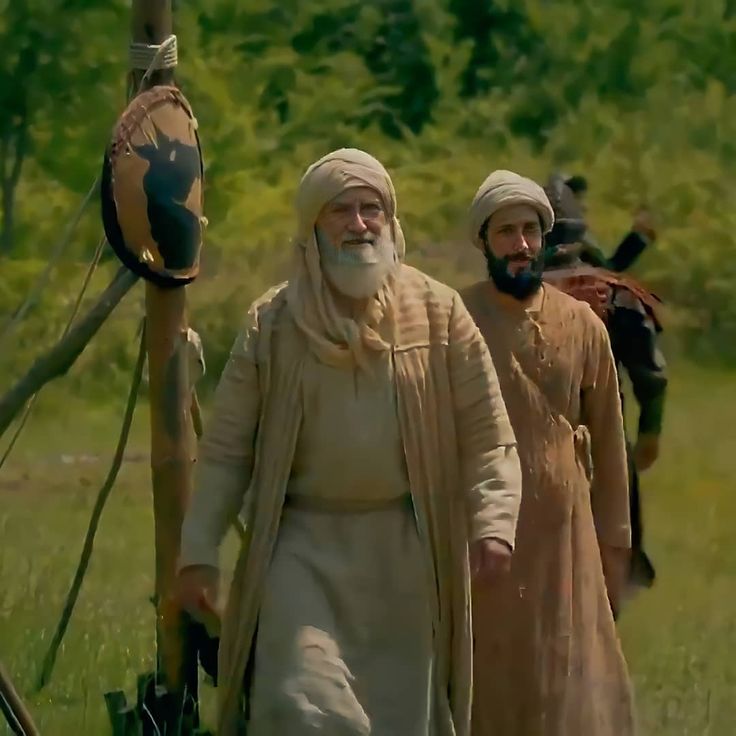 two men dressed in medieval clothing walking through a field