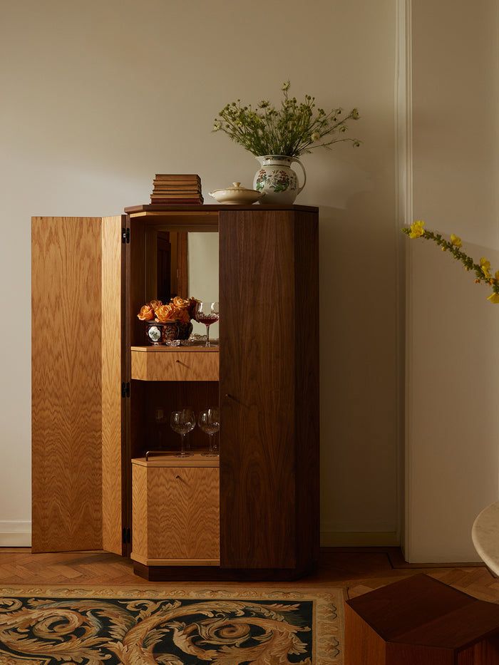 a wooden cabinet sitting next to a vase with flowers in it on top of a rug