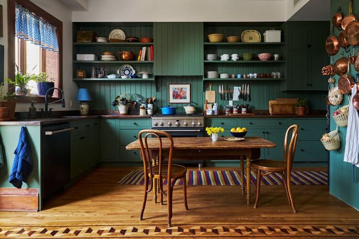 a kitchen with green cabinets and wooden floors, including a dining table surrounded by hanging pots and pans