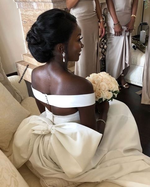 a woman sitting on a couch in front of a mirror wearing a white dress and holding a bouquet