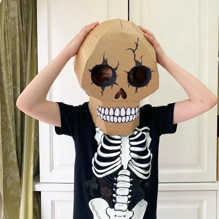 a young boy is holding up a cardboard skeleton mask