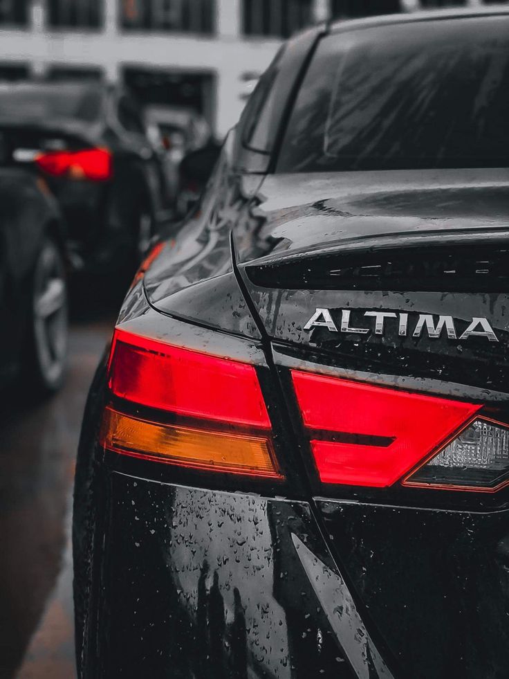 the back end of a black car parked in front of a white building on a rainy day