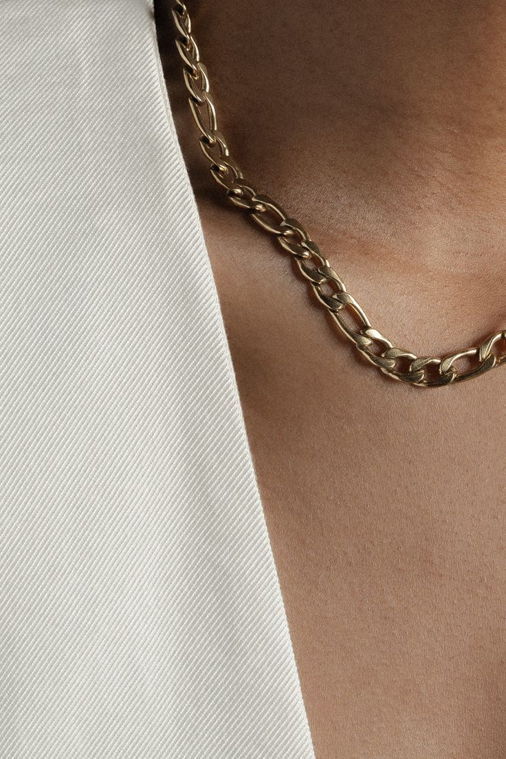 a close up of a person wearing a gold chain necklace on their left chest and white shirt on his right