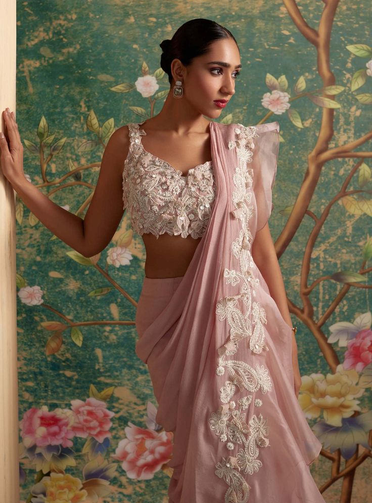 Elevate your ethnic elegance with this net embroidered sleeveless blouse paired flawlessly with an organza placement embroidered lehenga and complemented by an organza embroidered dupatta. The intricately embroidered lehenga boasts delicate ivory details and enchanting 3d florals, creating a set that exudes feminine grace. Perfect for special occasions and celebrations, this ensemble effortlessly blends tradition with contemporary style. Immerse yourself in the exquisite craftsmanship and timele Crop Blouse Designs, Saree Chiffon, Pink Sari, Ridhi Mehra, Floral Saree, Ruffle Saree, Padded Blouse, Saree Designs Party Wear, Indian Dresses Traditional