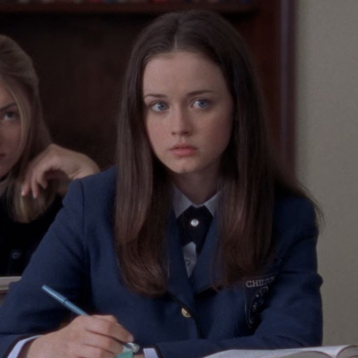 two women sitting at a desk in front of an open book and writing on paper