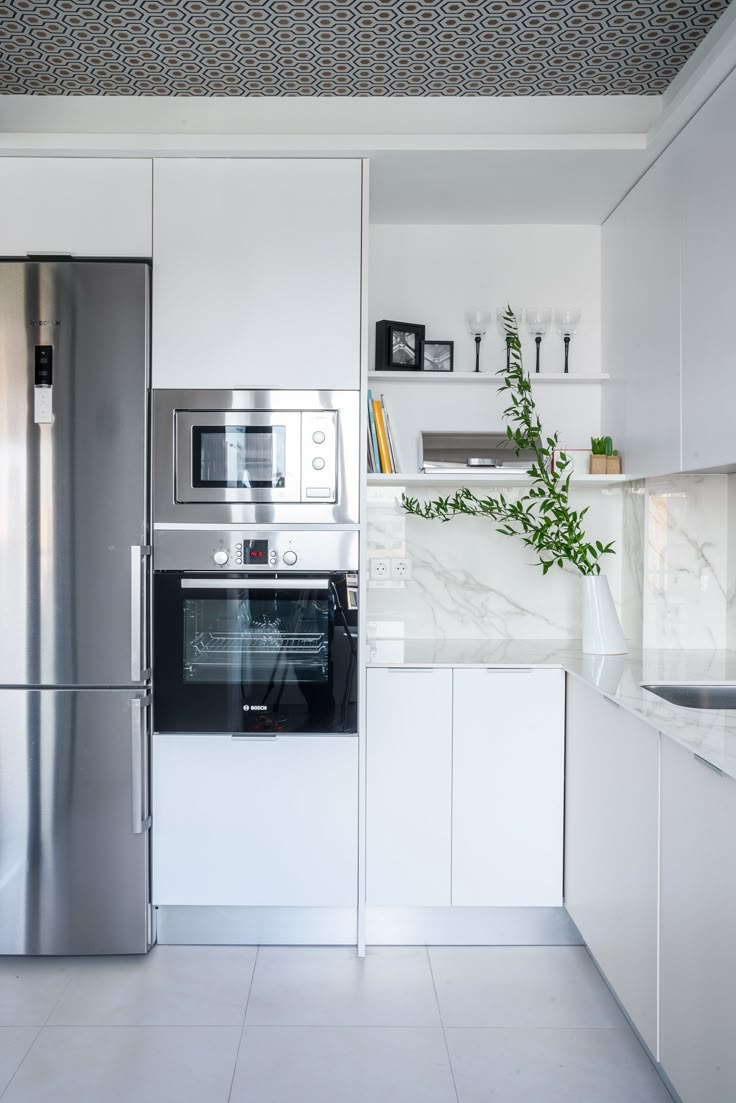 a modern kitchen with stainless steel appliances and white cabinetry, along with marble countertops