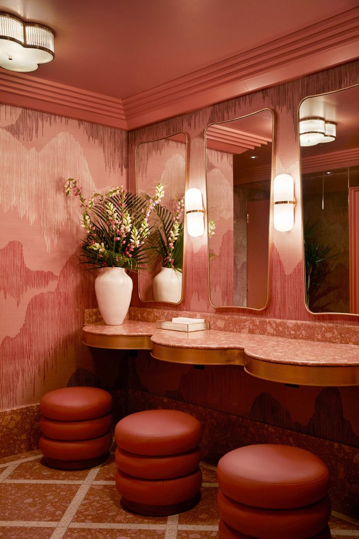 a pink bathroom with stools and mirrors