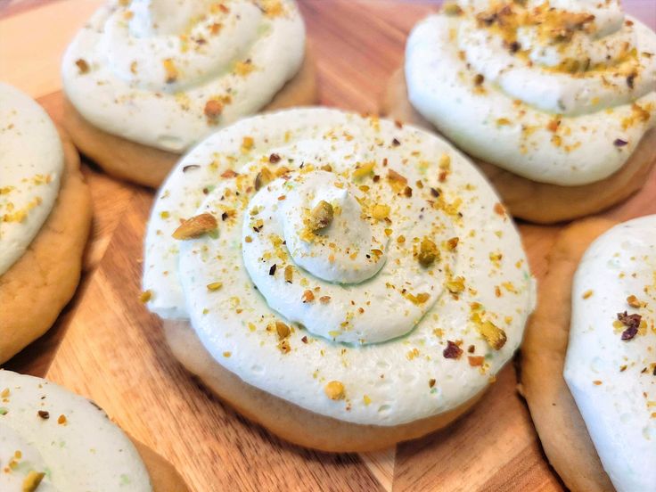 some cookies with white frosting and sprinkles are on a wooden board