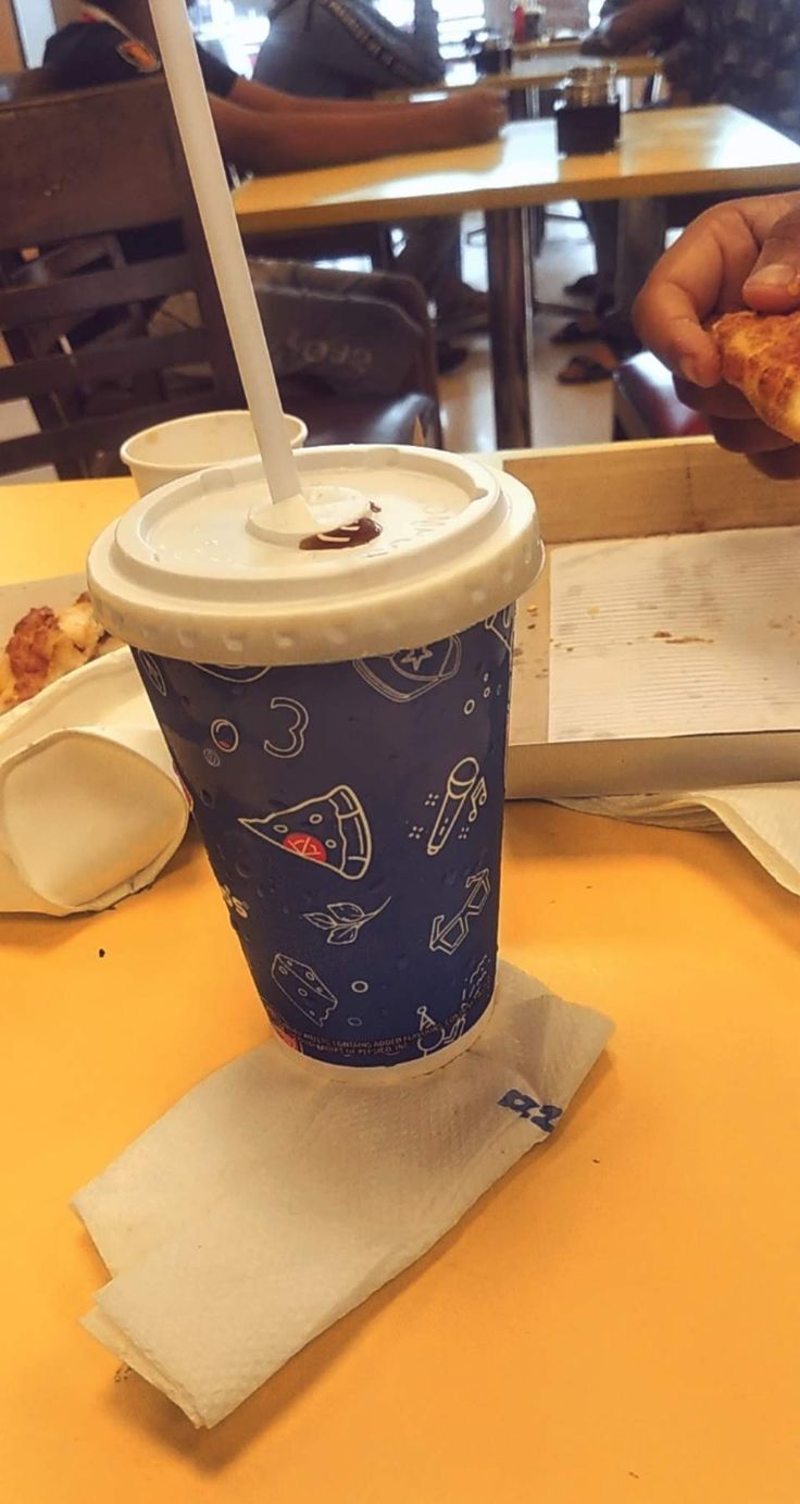 a person holding up a piece of pizza in front of a cup with a straw